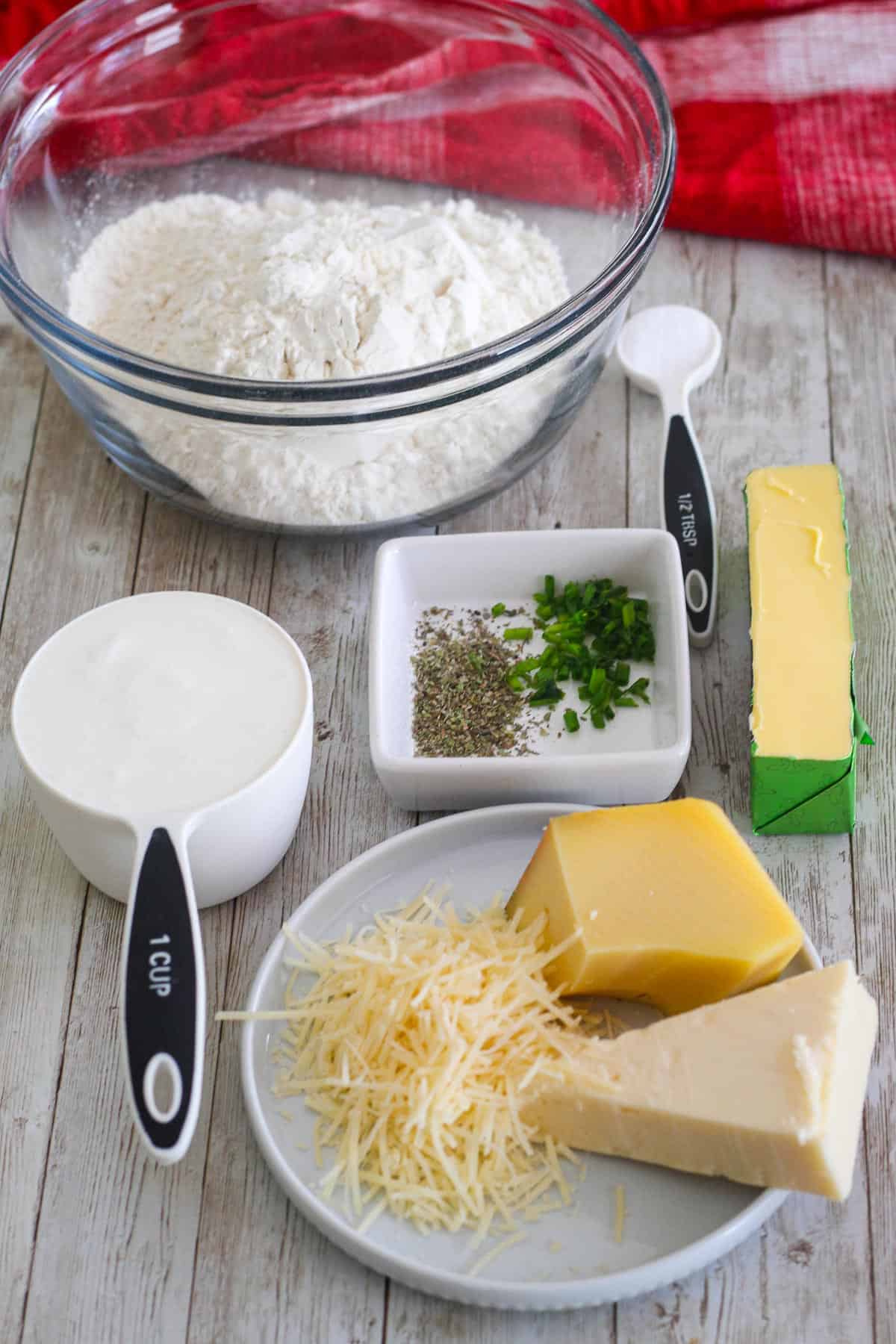 Ingredients to make three cheese biscuits all together: flour, baking soda, chives, seasonings, butter, buttermilk, jarlsberg cheese, parmesan cheese, asiago cheese.