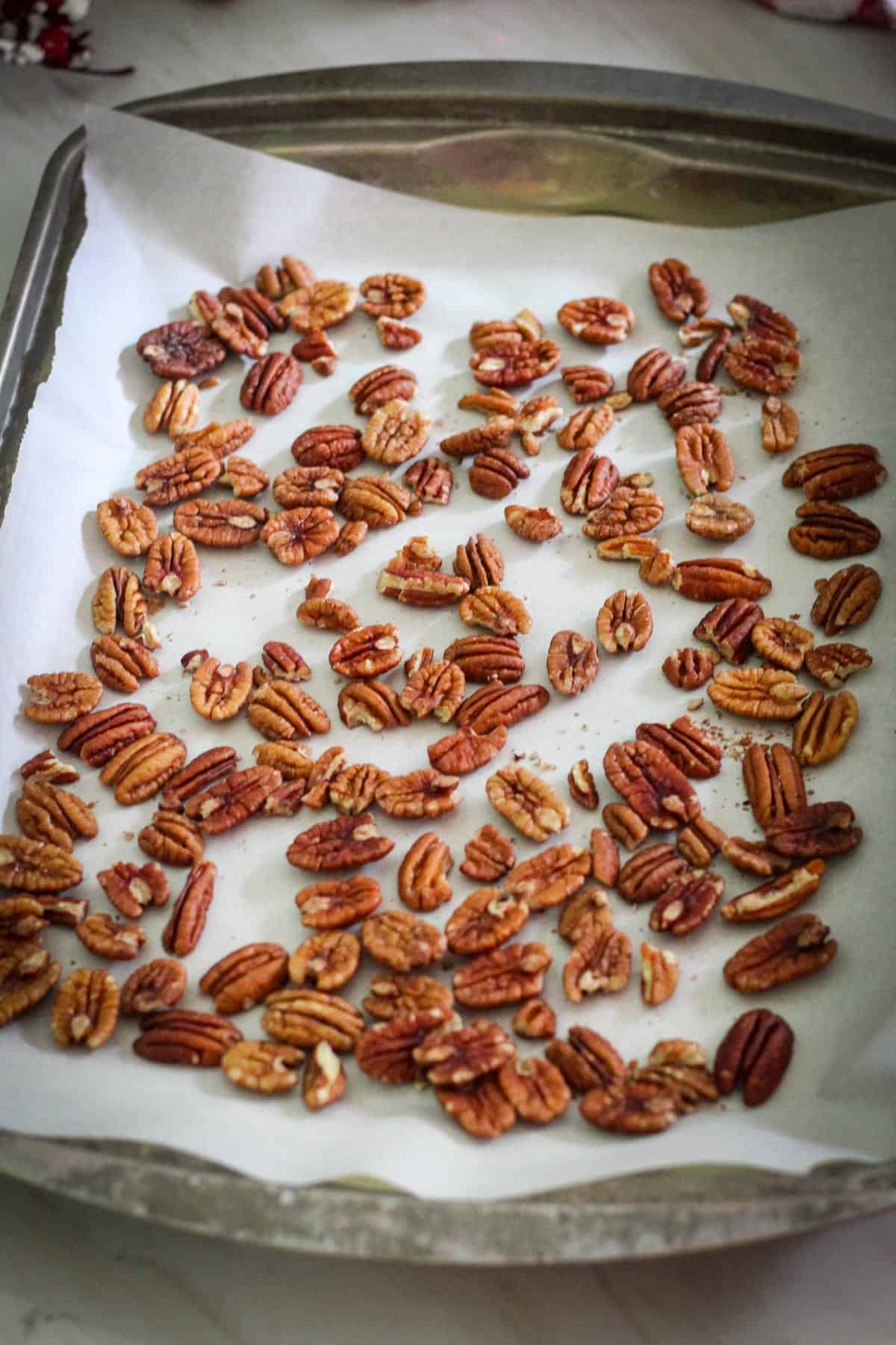 Pecans over parchment paper in a baking sheet.
