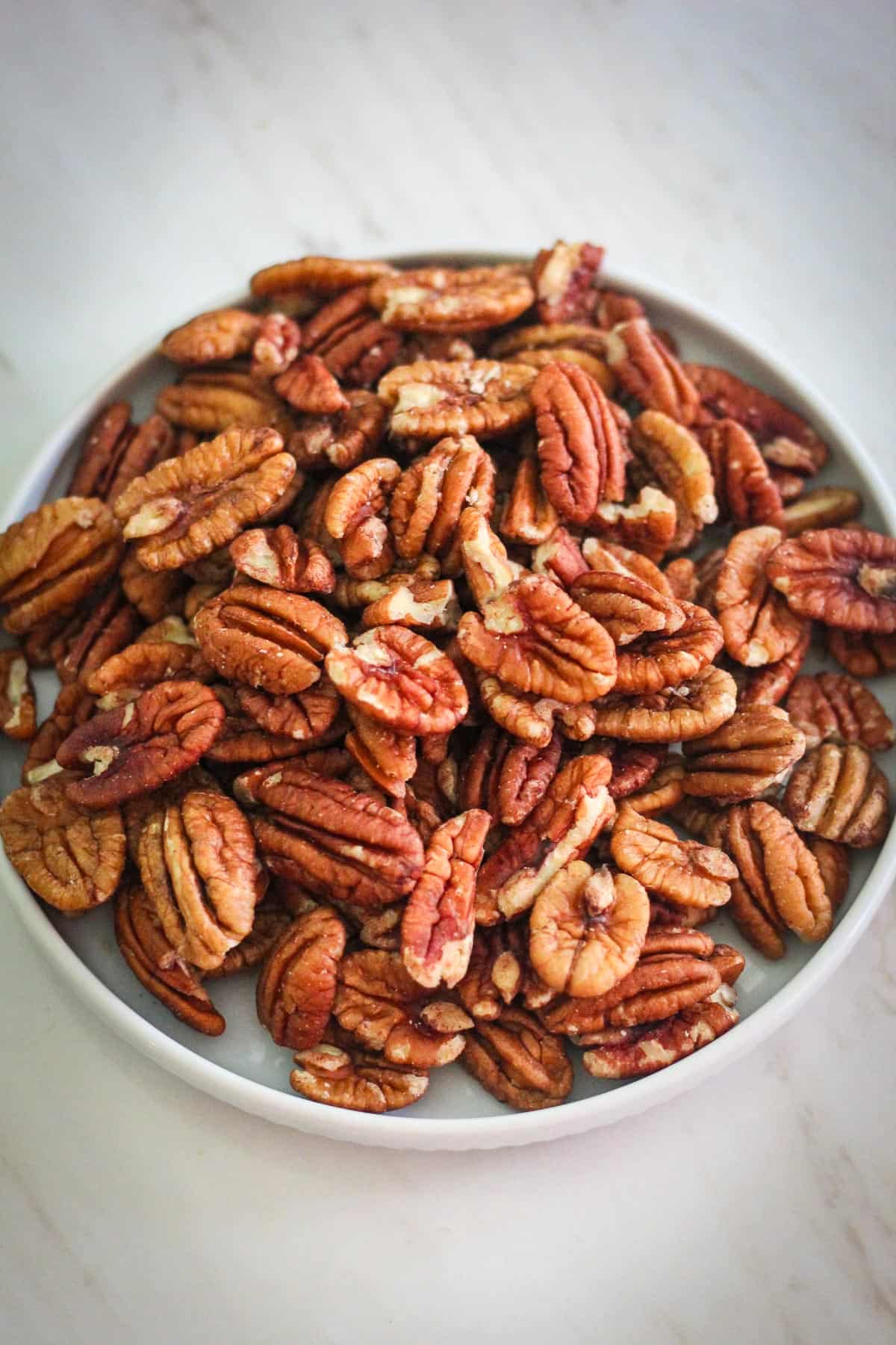 Raw pecan halves on a round plate.