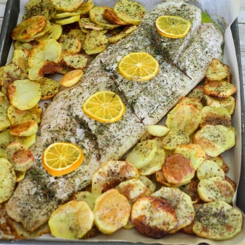 A baking sheet showing baked corvina with roasted potatoes.
