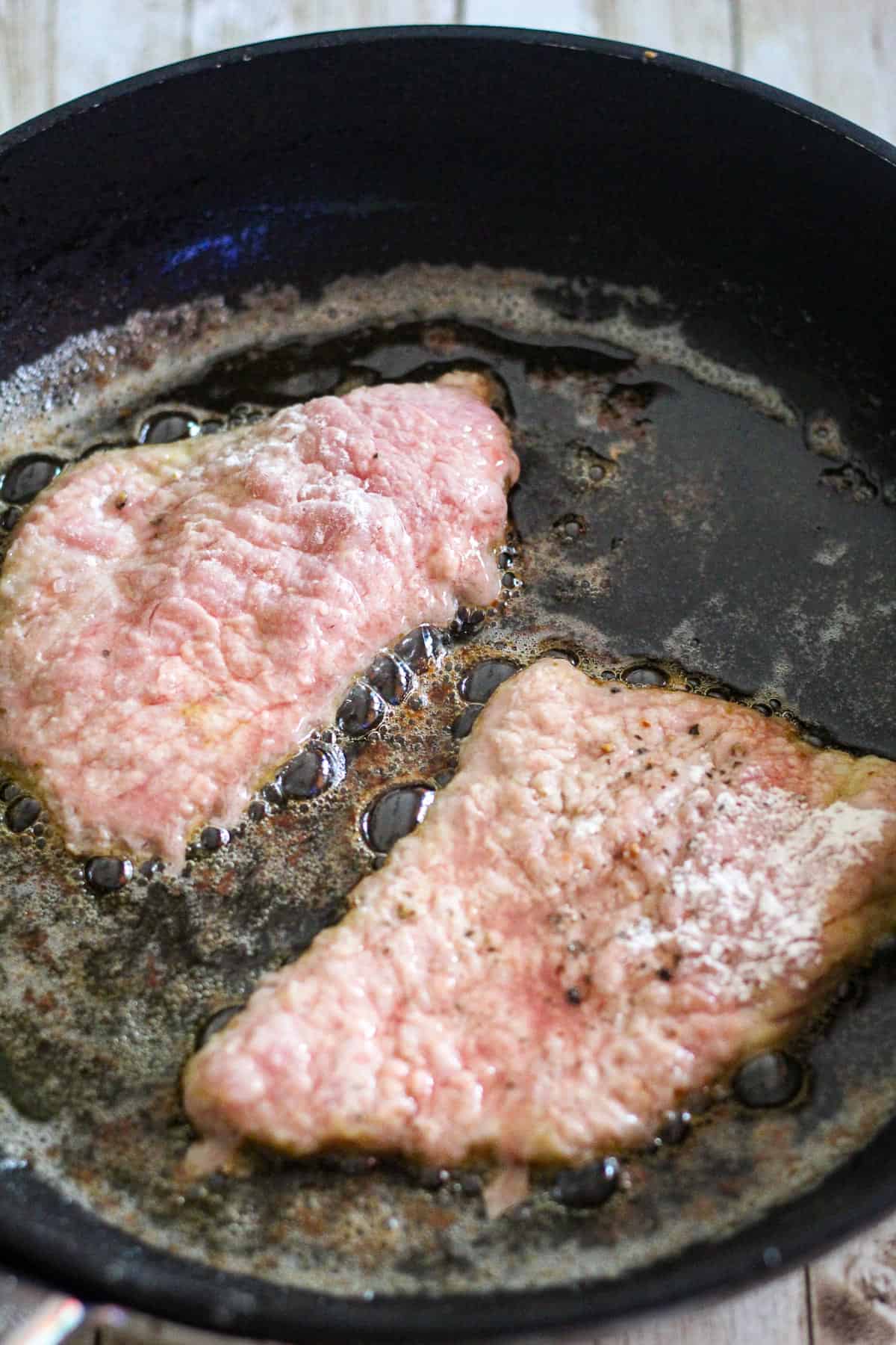 Skillet showing veal cutlets searing.