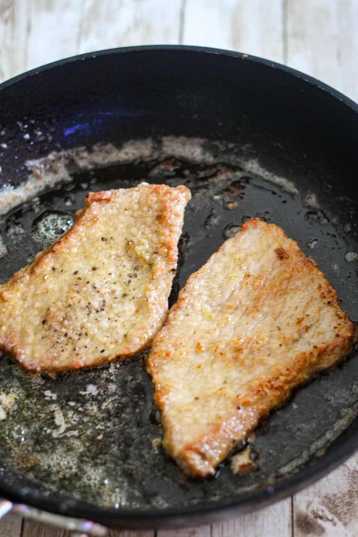 Skillet showing veal cutlets searing.