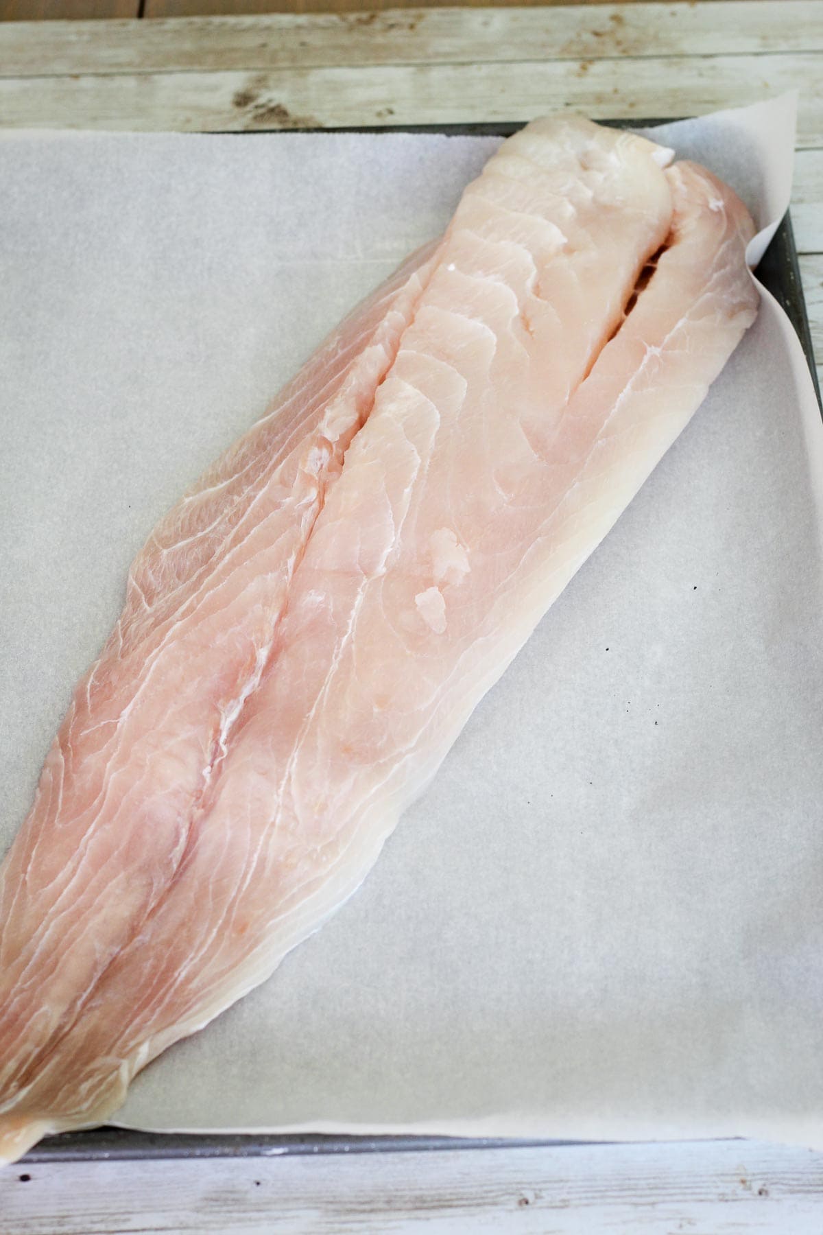 Raw corvina fillet over parchment paper on a baking sheet.