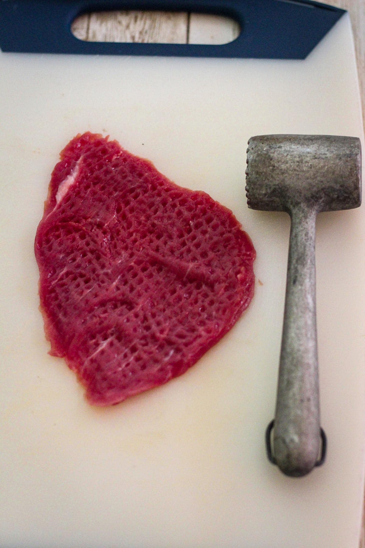 A veal cutlet on a cutting board, visually pounded shown next to a meat mallet.