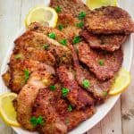 A platter with veal scallopini, garnished with lemon slices and parsley.