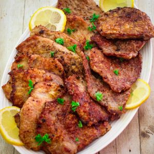 A platter with veal scallopini, garnished with lemon slices and parsley.