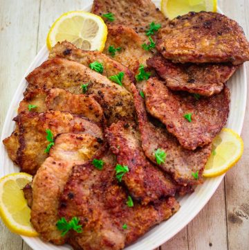 A platter with veal scallopini, garnished with lemon slices and parsley.