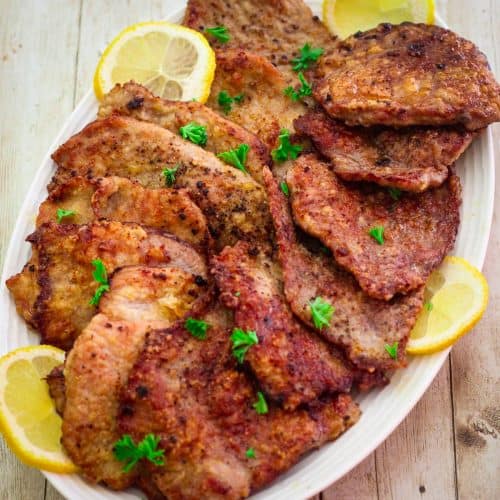 A platter with veal scallopini, garnished with lemon slices and parsley.