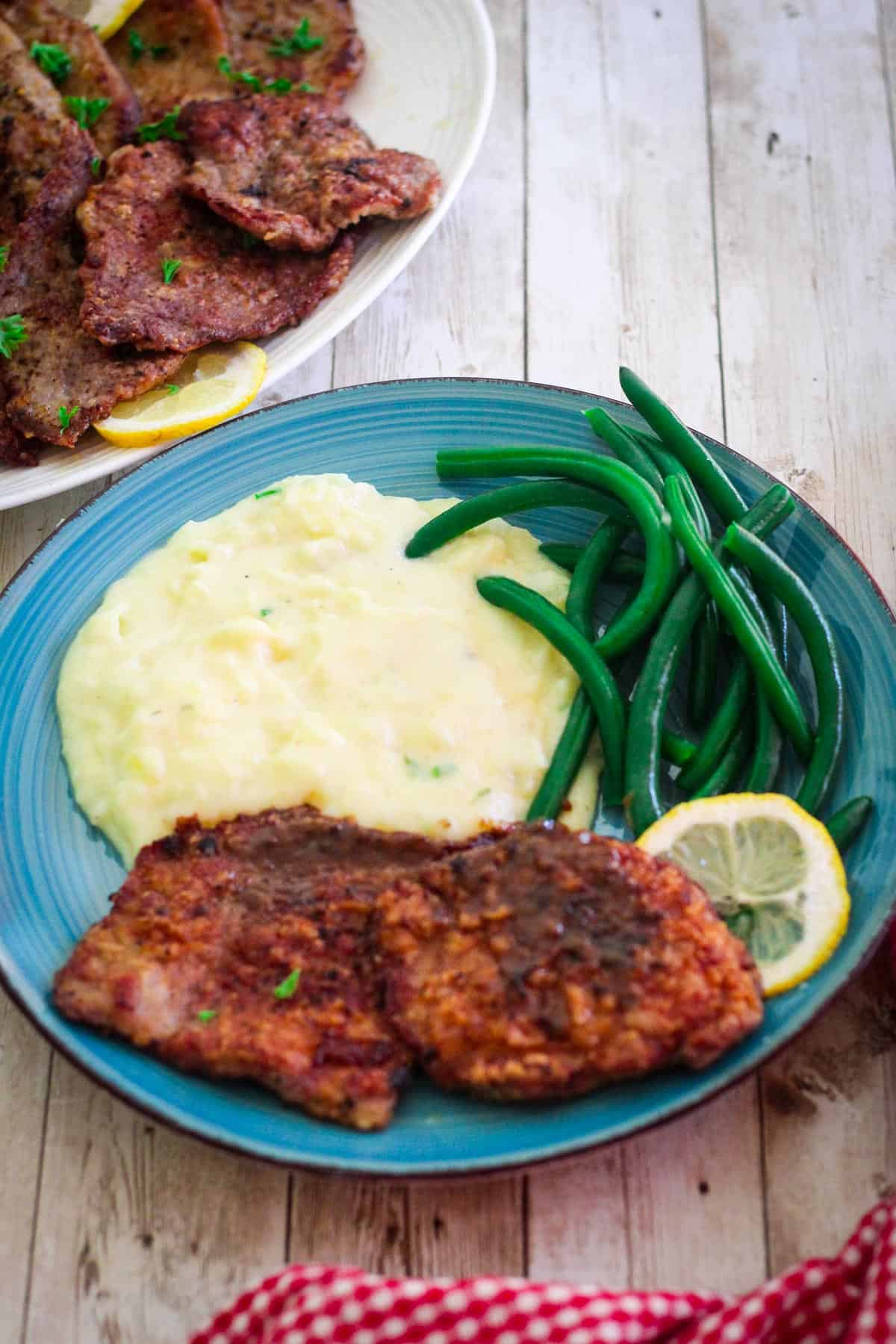 A dinner plate with veal scallopini served with mashed potatoes and green beans.