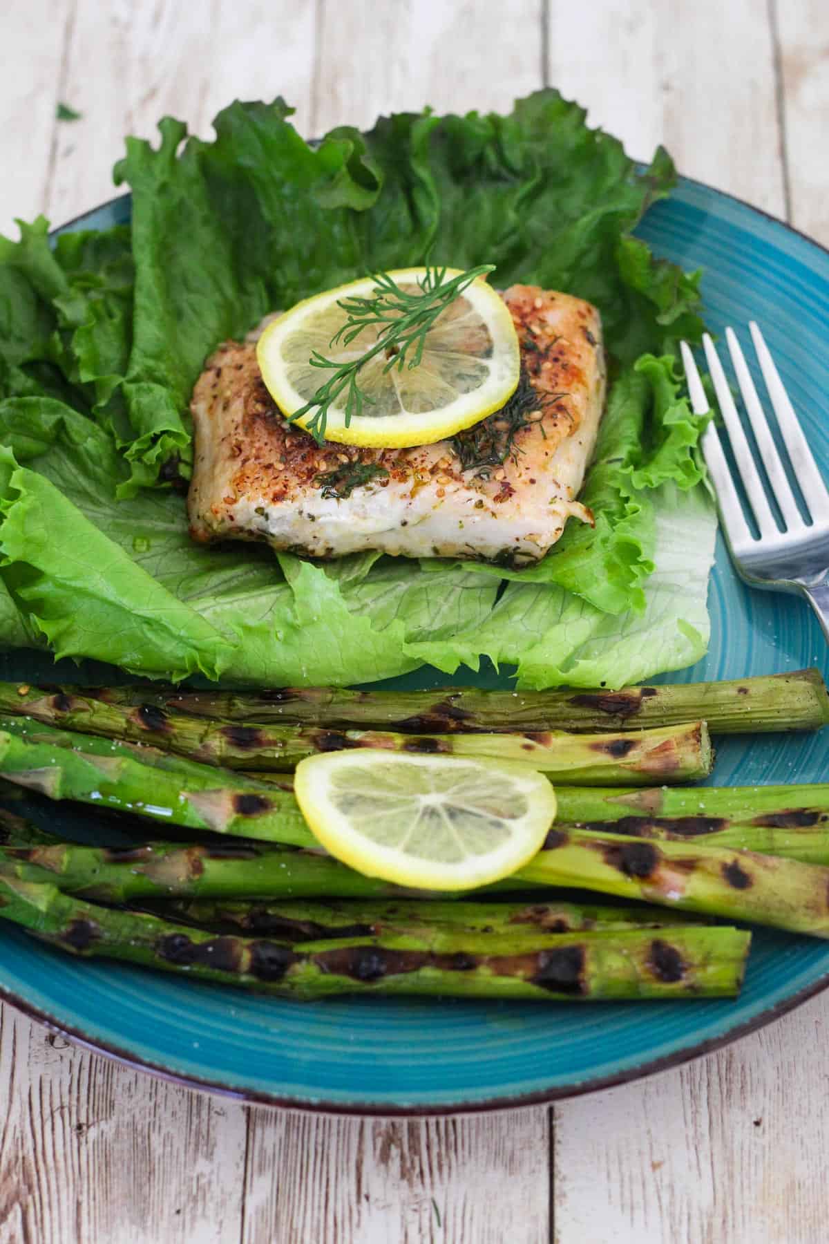 A dinner plate with mahi mahi, topped with lemon and dill - served over lettuce and next to grilled asparagus. 