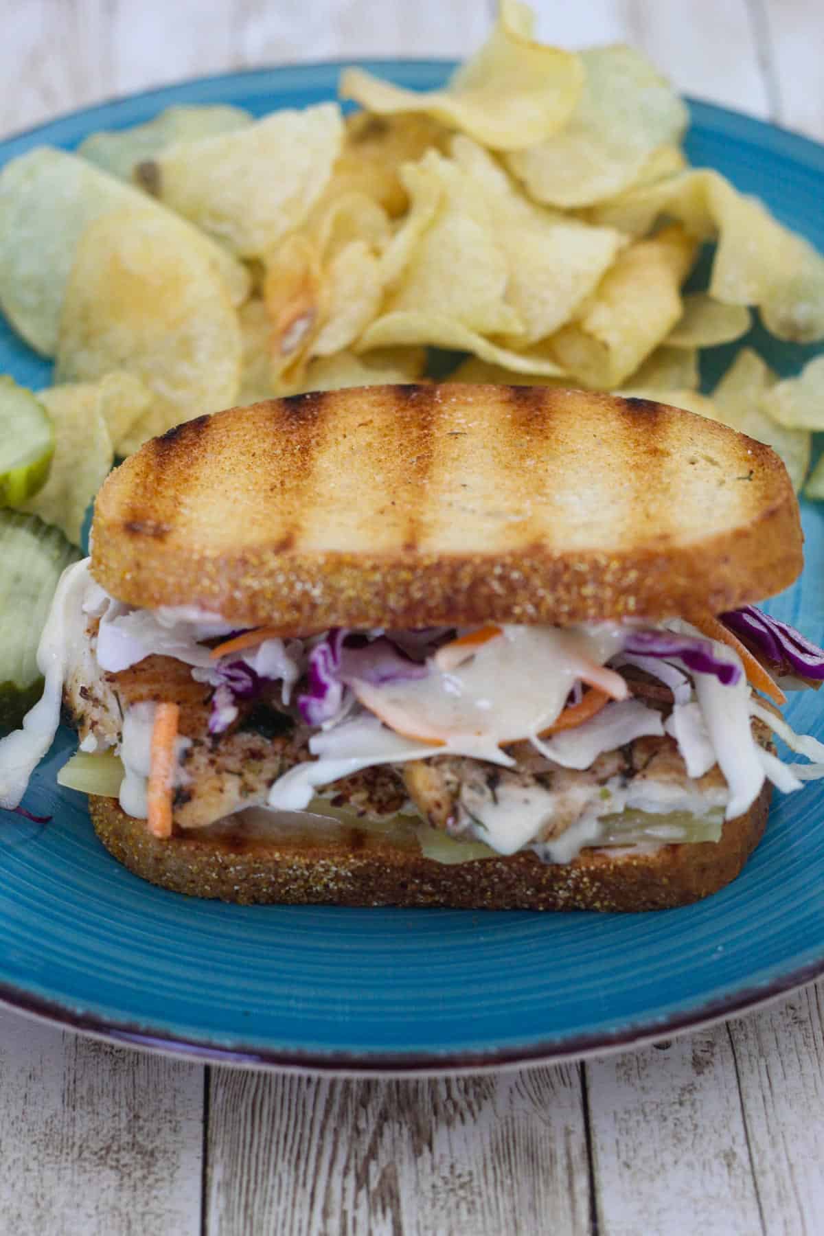 A platter with a reuben sandwich made with mahi mahi, served with chips and pickles.
