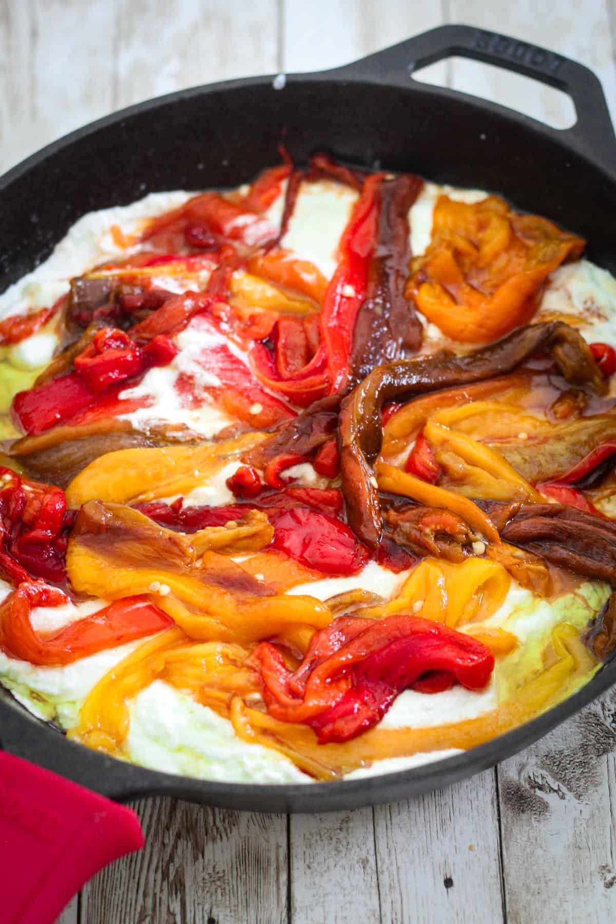 Adding peppers over the ricotta sauce in the cast iron skillet.