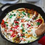 A cast iron skillet showing a dish made with peppers and ricotta sauce.