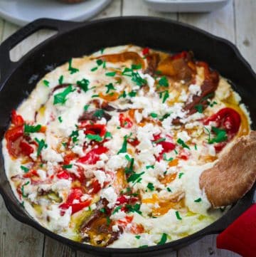 A cast iron skillet showing a dish made with peppers and ricotta sauce.