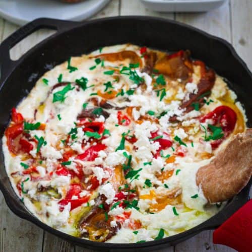 A cast iron skillet showing a dish made with peppers and ricotta sauce.