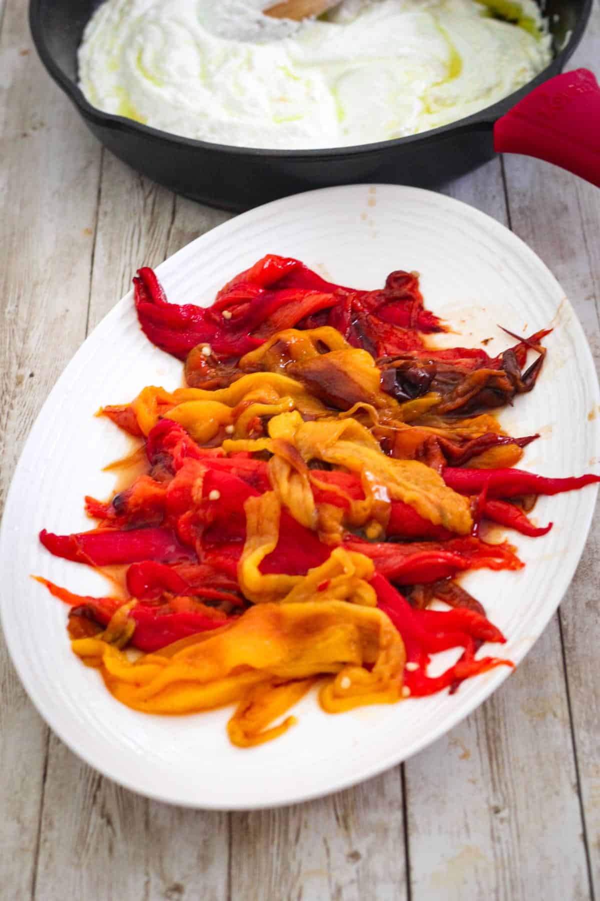 Stripped roasted peppers in a plate after they have been peeled. Cast iron skillet is in the background with a ricotta sauce in it.